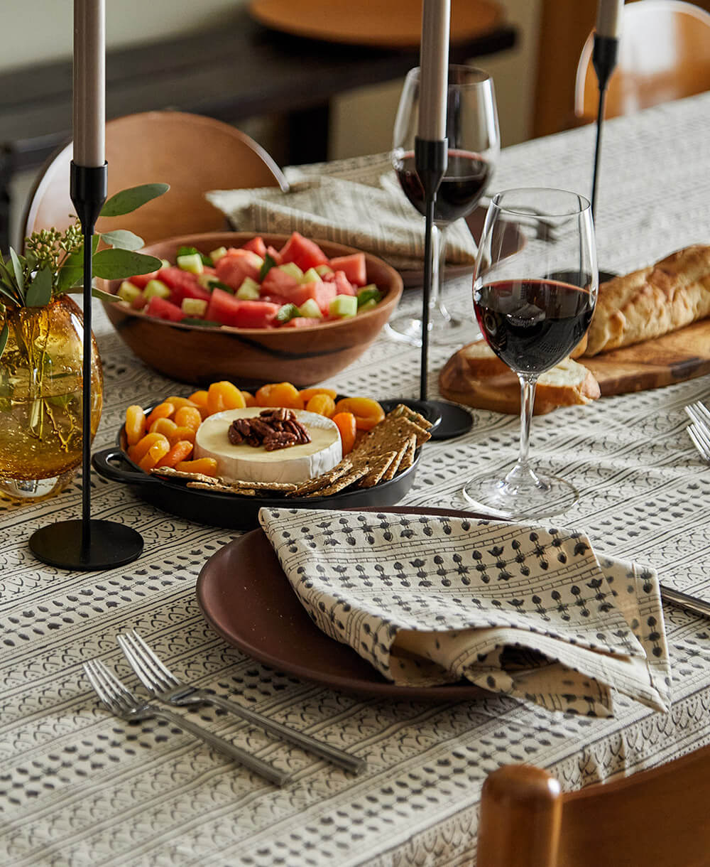 Dining table set with wine, cheese, and fruit platter on a patterned tablecloth