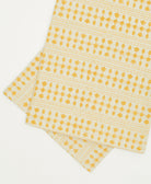 Two yellow patterned cloth napkins stacked on a white background