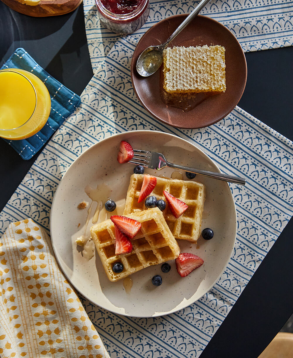 Plate of waffles with strawberries and blueberries on a patterned tablecloth