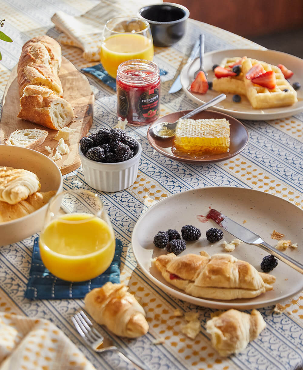 Breakfast table with pastries, fruit, and drinks on a patterned tablecloth