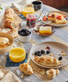 Breakfast table with pastries, fruit, and drinks on a patterned tablecloth