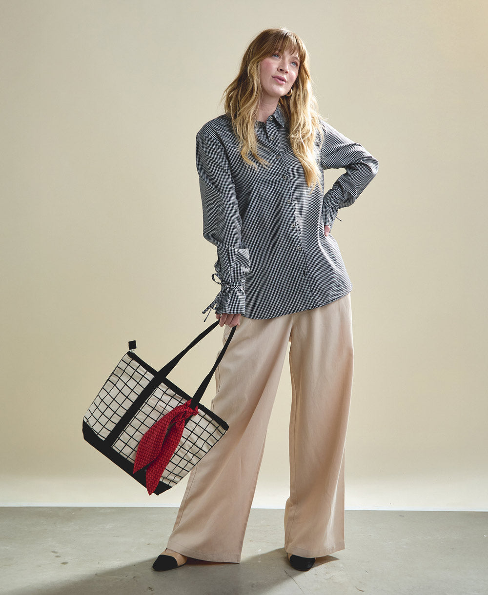 woman carrying block print grid mini tote bag by the handle in black and white