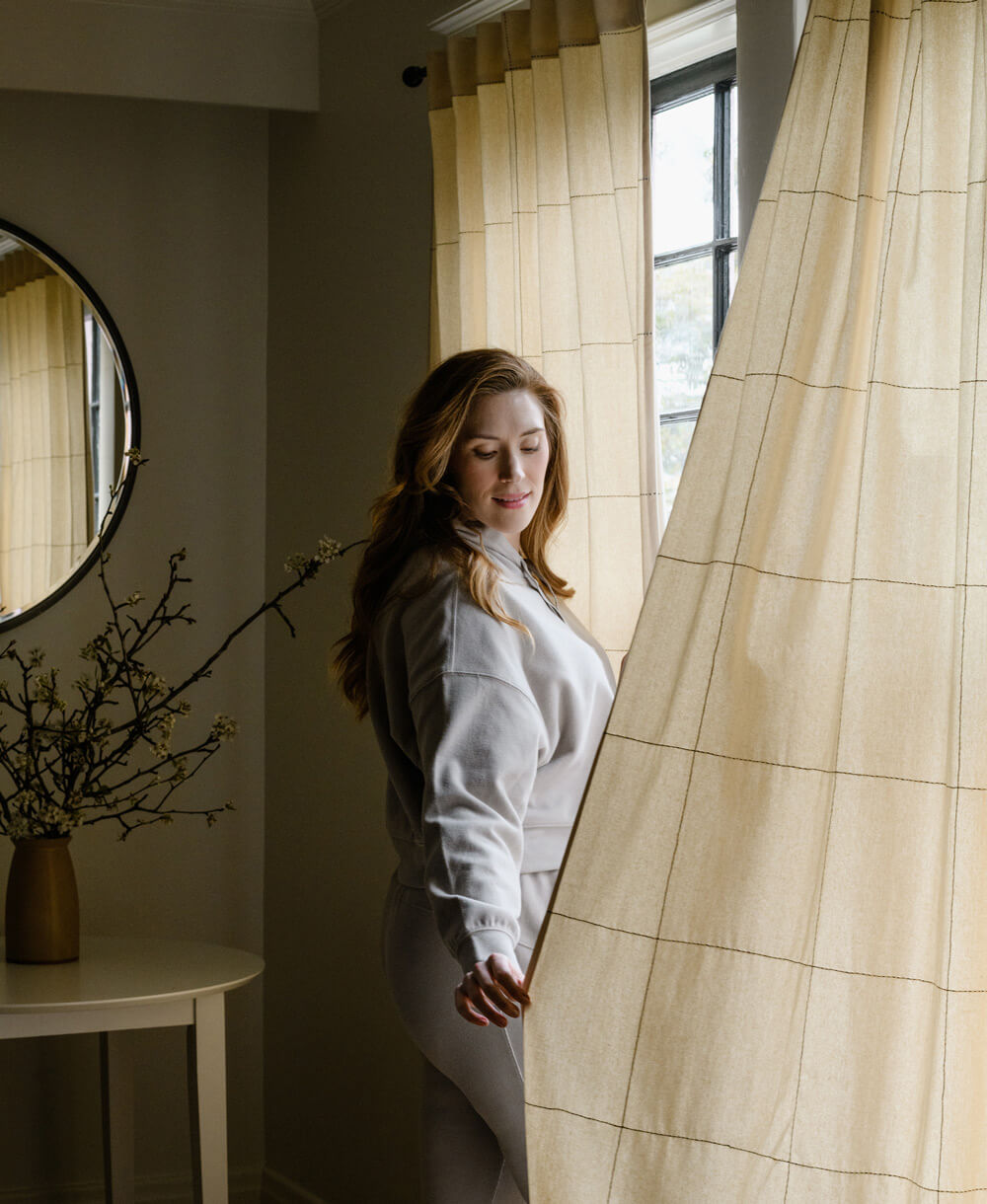 Woman standing in a room with curtains and a mirror