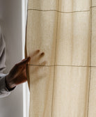 Hand touching a beige curtain with an embroidered grid pattern