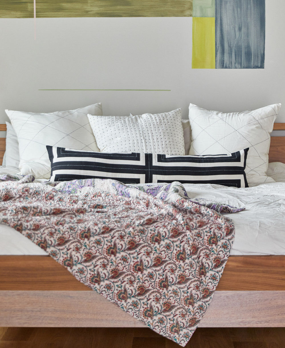 Bed with unique kantha quilt and a long lumbar pillow against a wall with abstract art