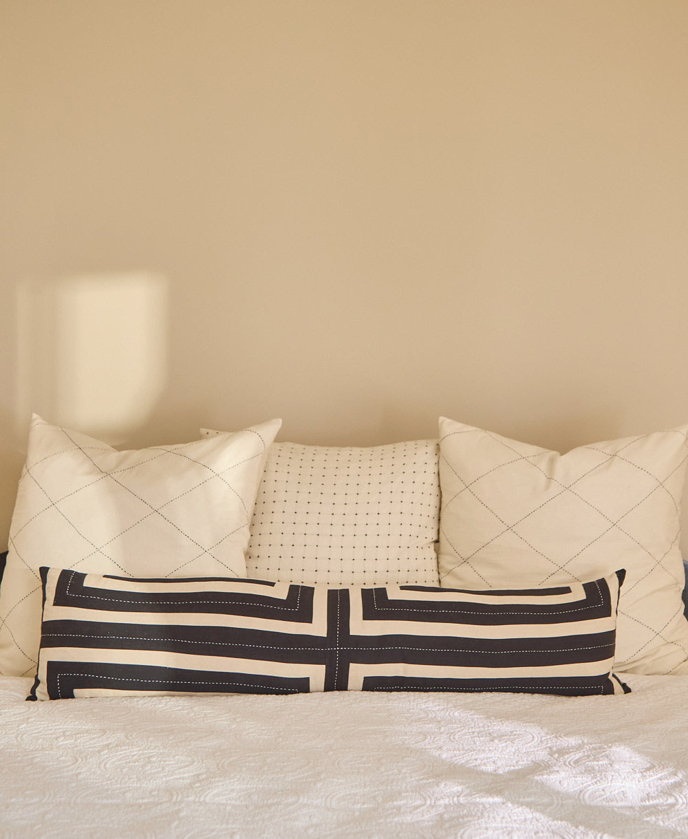 black and white long lumbar pillow on all white bed with coordinating white pillows