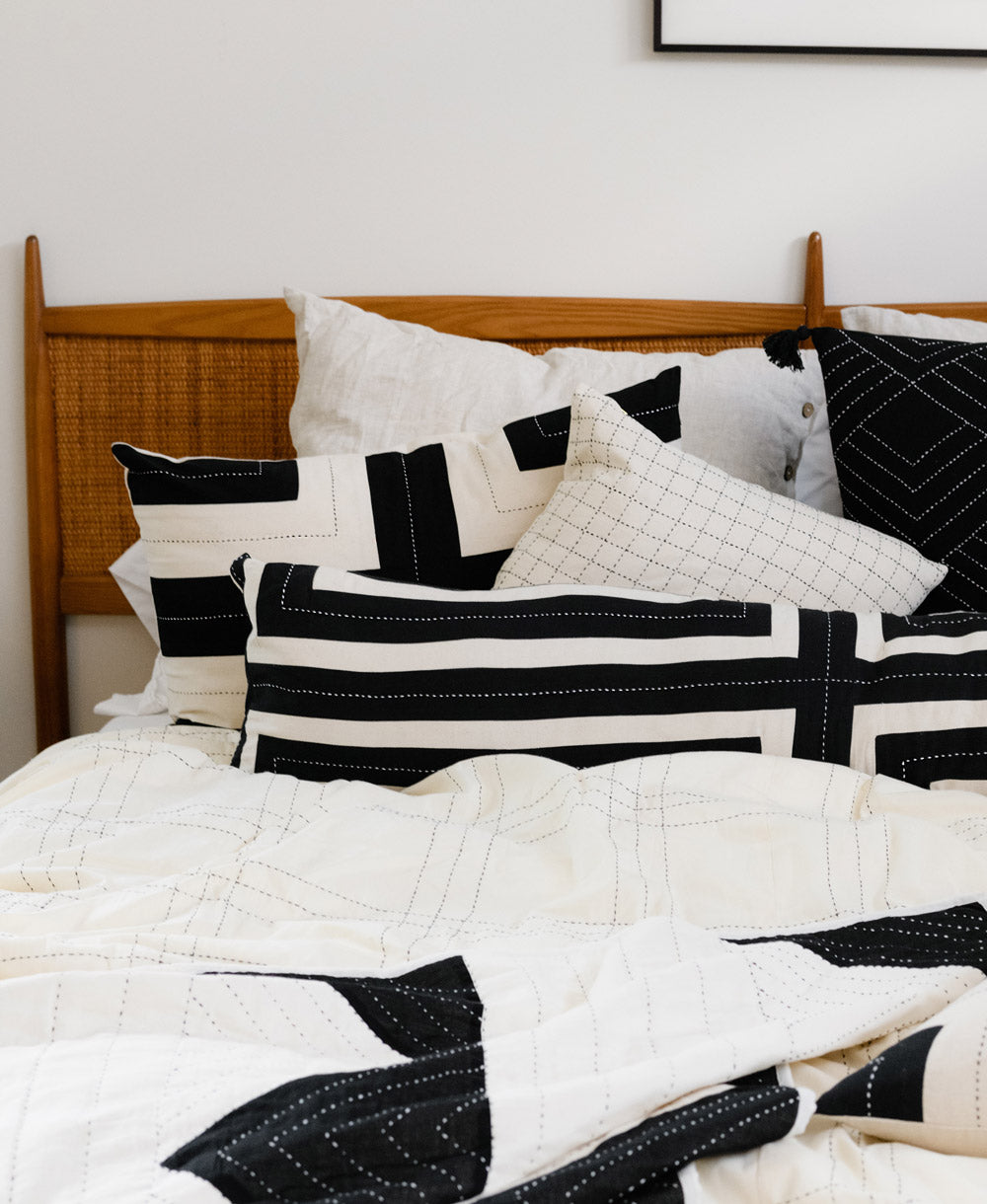 Bed with black and white patterned pillows and quilt with a wooden headboard