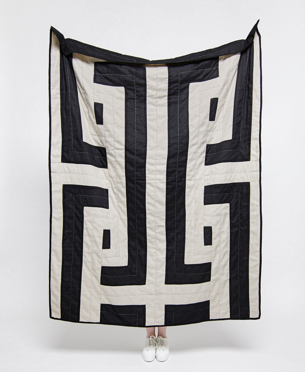Black and white patterned quilt draped over a person on a white background