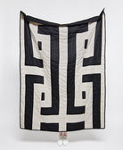 Black and white patterned quilt draped over a person on a white background
