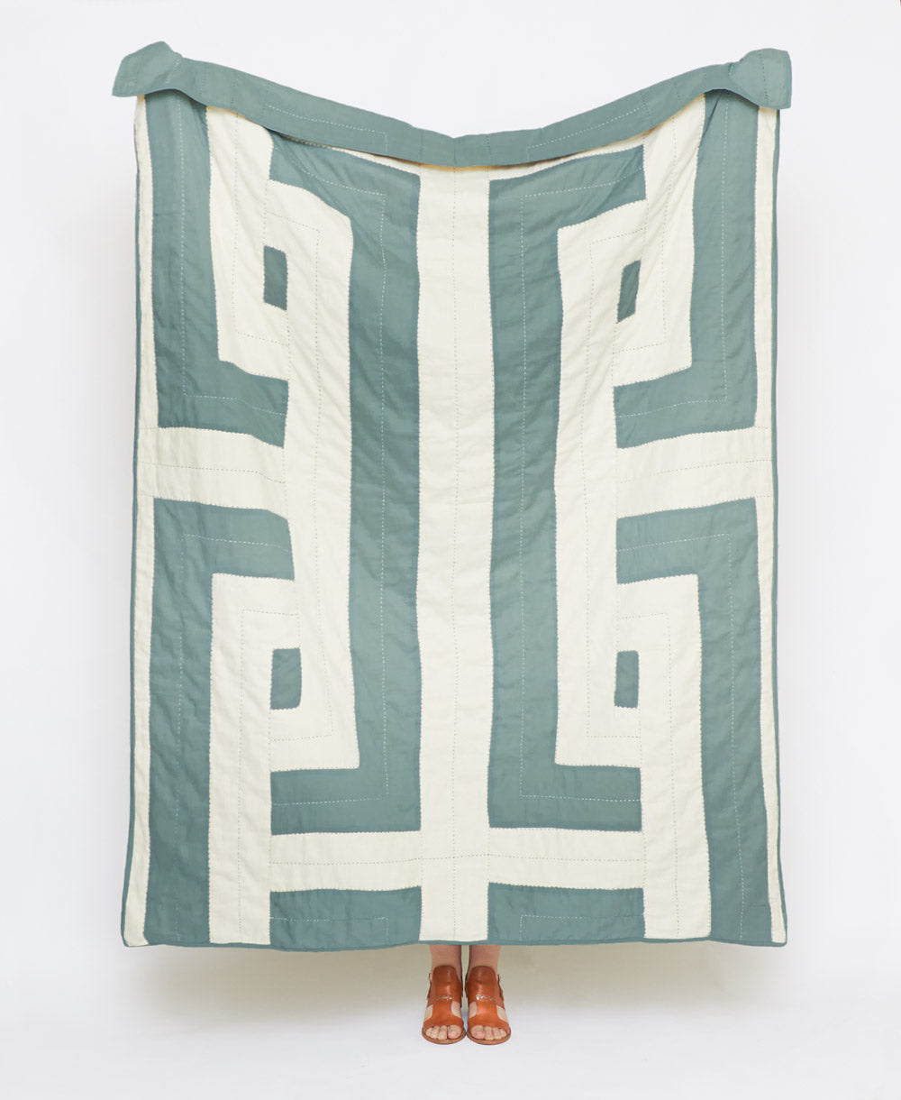 Quilt with geometric pattern draped over a person on a white background