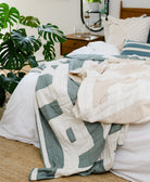 Quilted blanket on a bed with pillows and a plant in the background