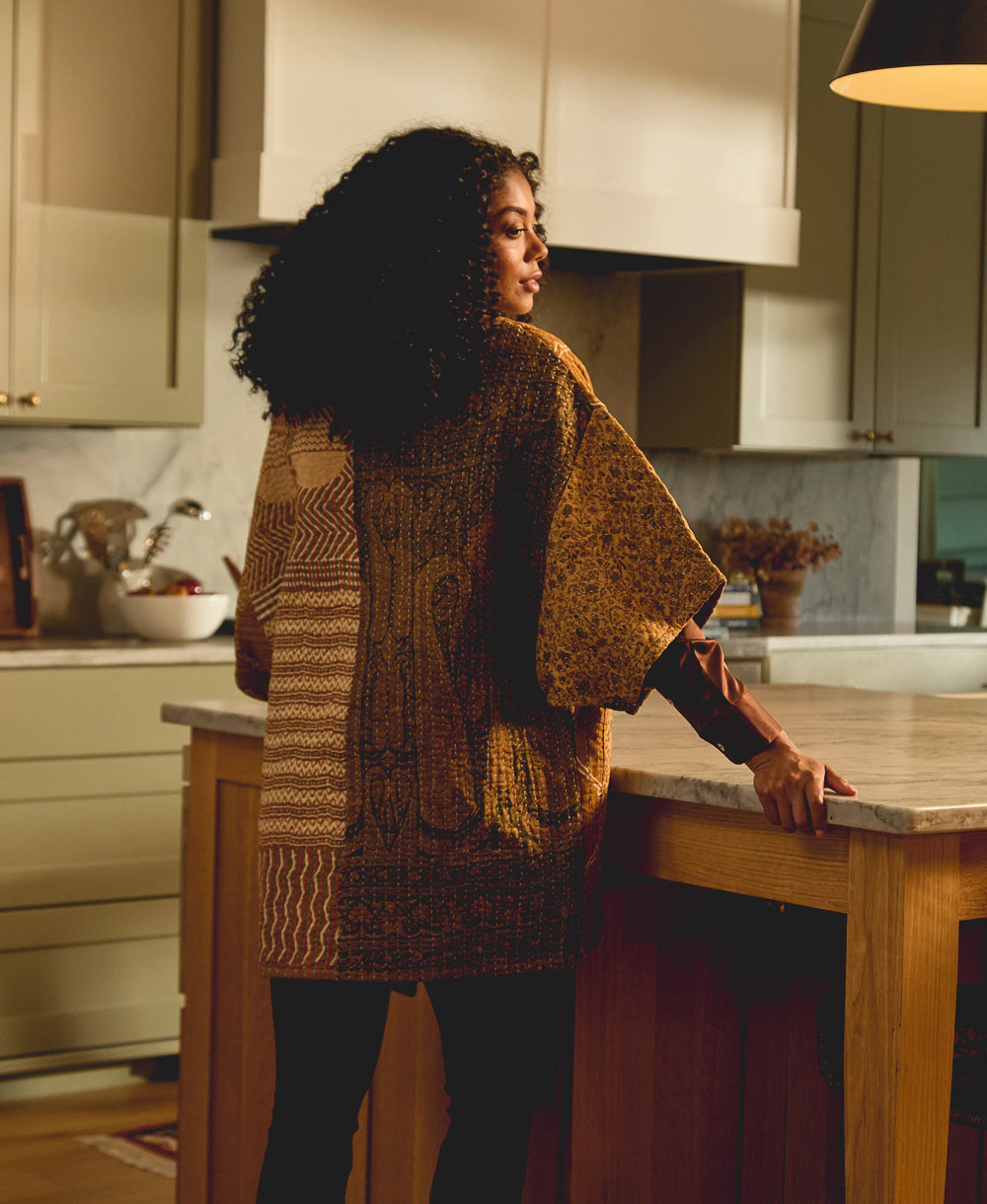 woman standing in a modern kitchen wearing a quilted jacket showing off the back pattern