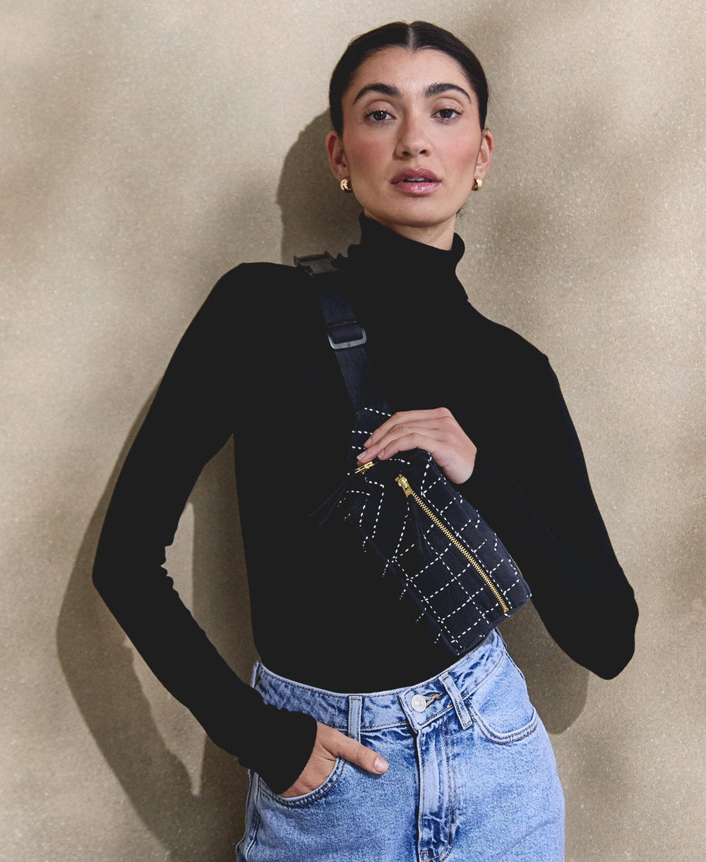 Woman wearing a black turtleneck sweater and blue jeans against a beige wall.