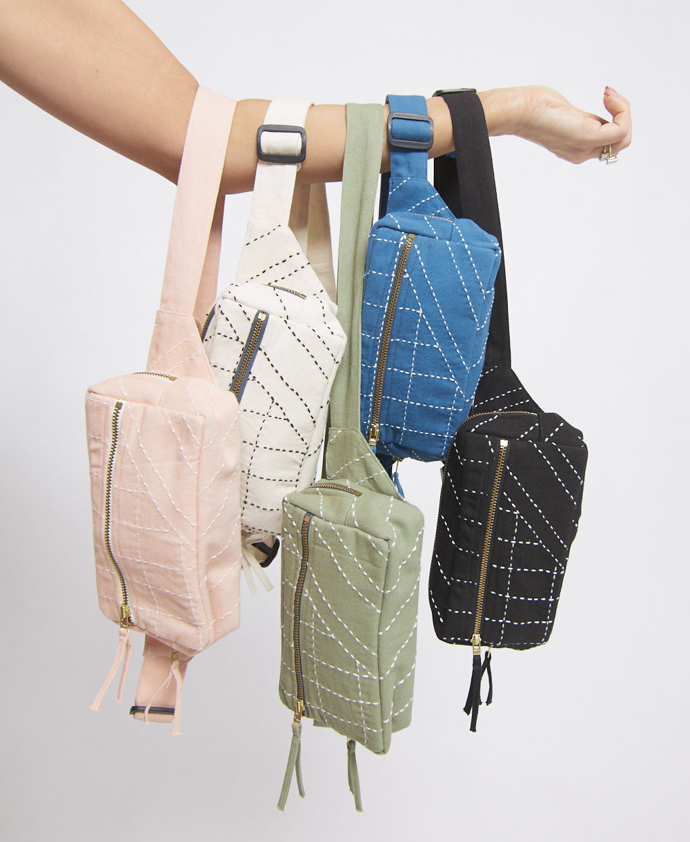 Five small belt bags in different colors hanging from a person's arm against a light gray background.