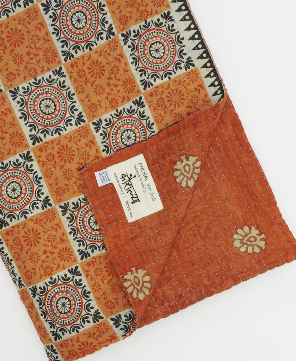 kantha quilt throw with a tag featuring the hand-stitched signature of the maker