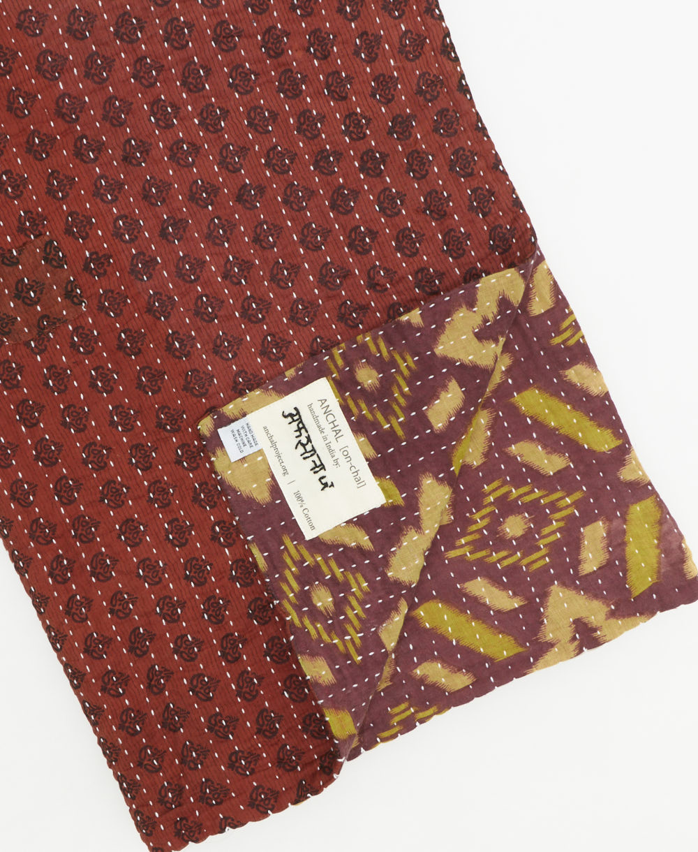 kantha quilt throw with a tag featuring the hand-stitched signature of the maker