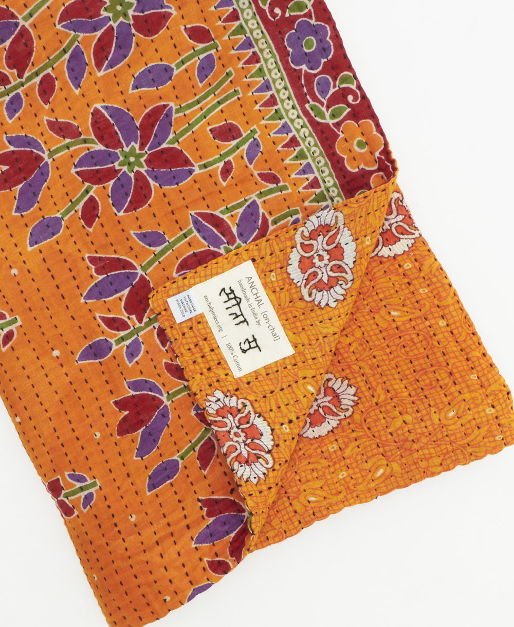 kantha quilt throw with a tag featuring the hand-stitched signature of the maker
