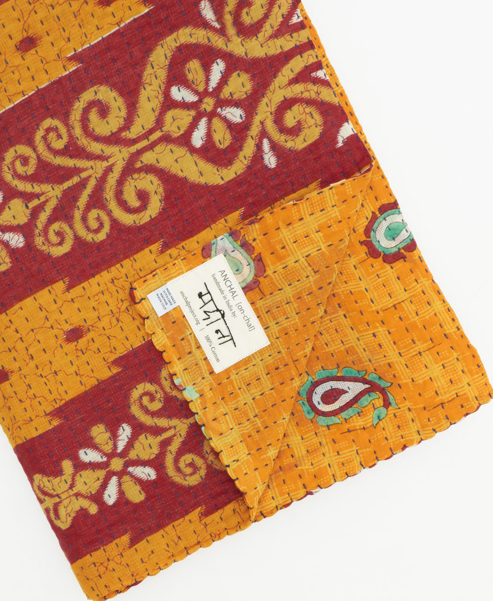 kantha quilt throw with a tag featuring the hand-stitched signature of the maker