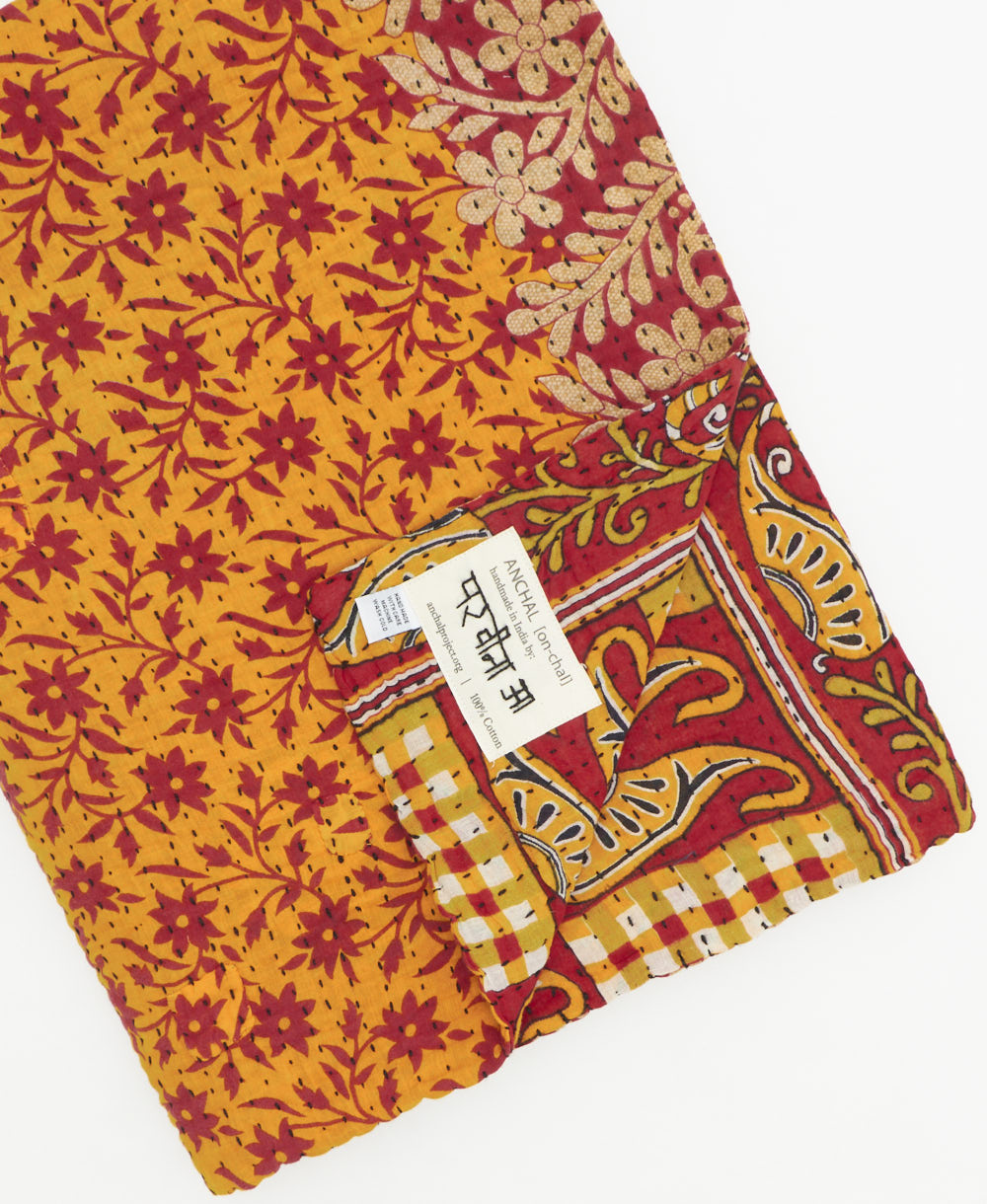 kantha quilt throw with a tag featuring the hand-stitched signature of the maker