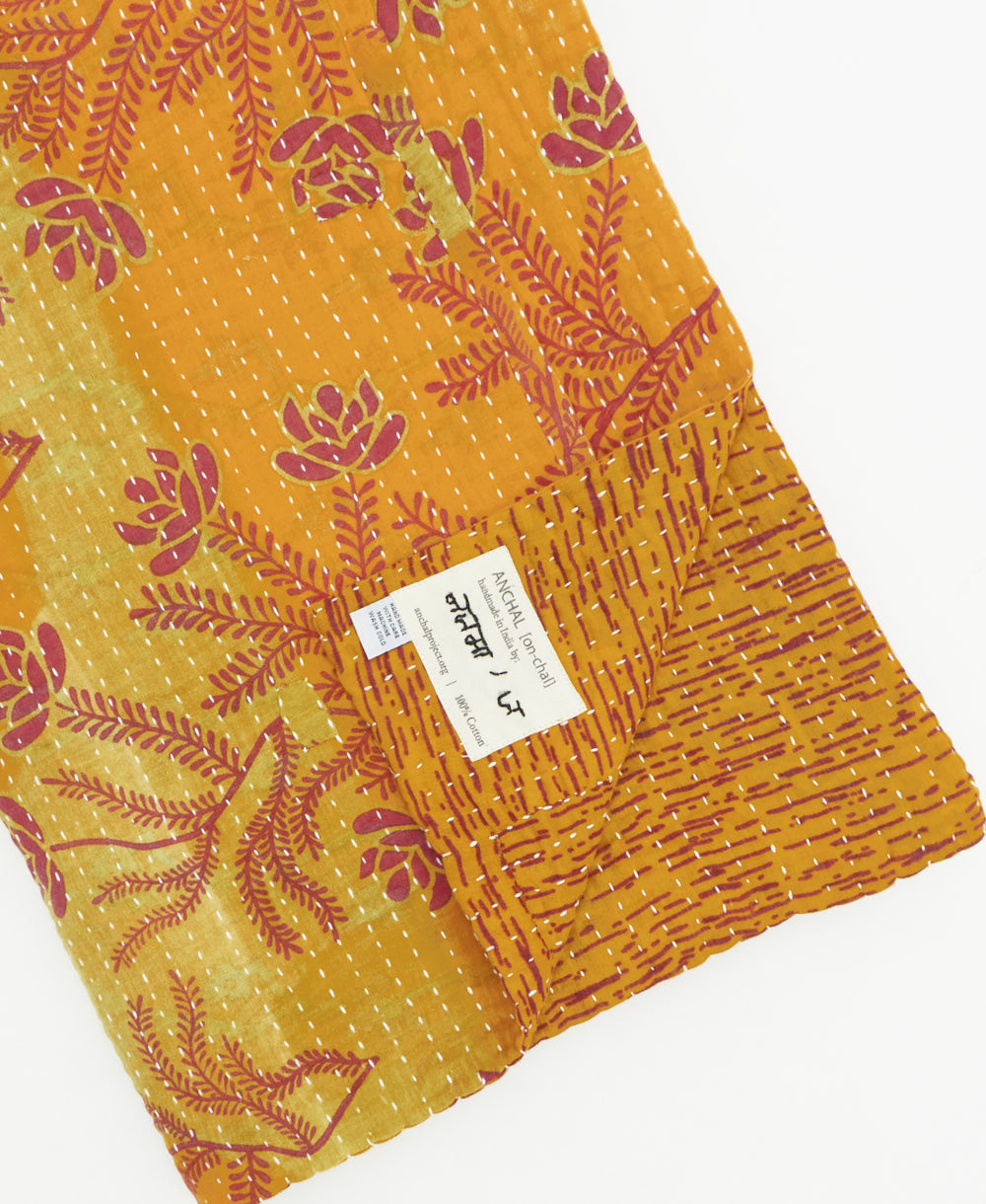 kantha quilt throw with a tag featuring the hand-stitched signature of the maker