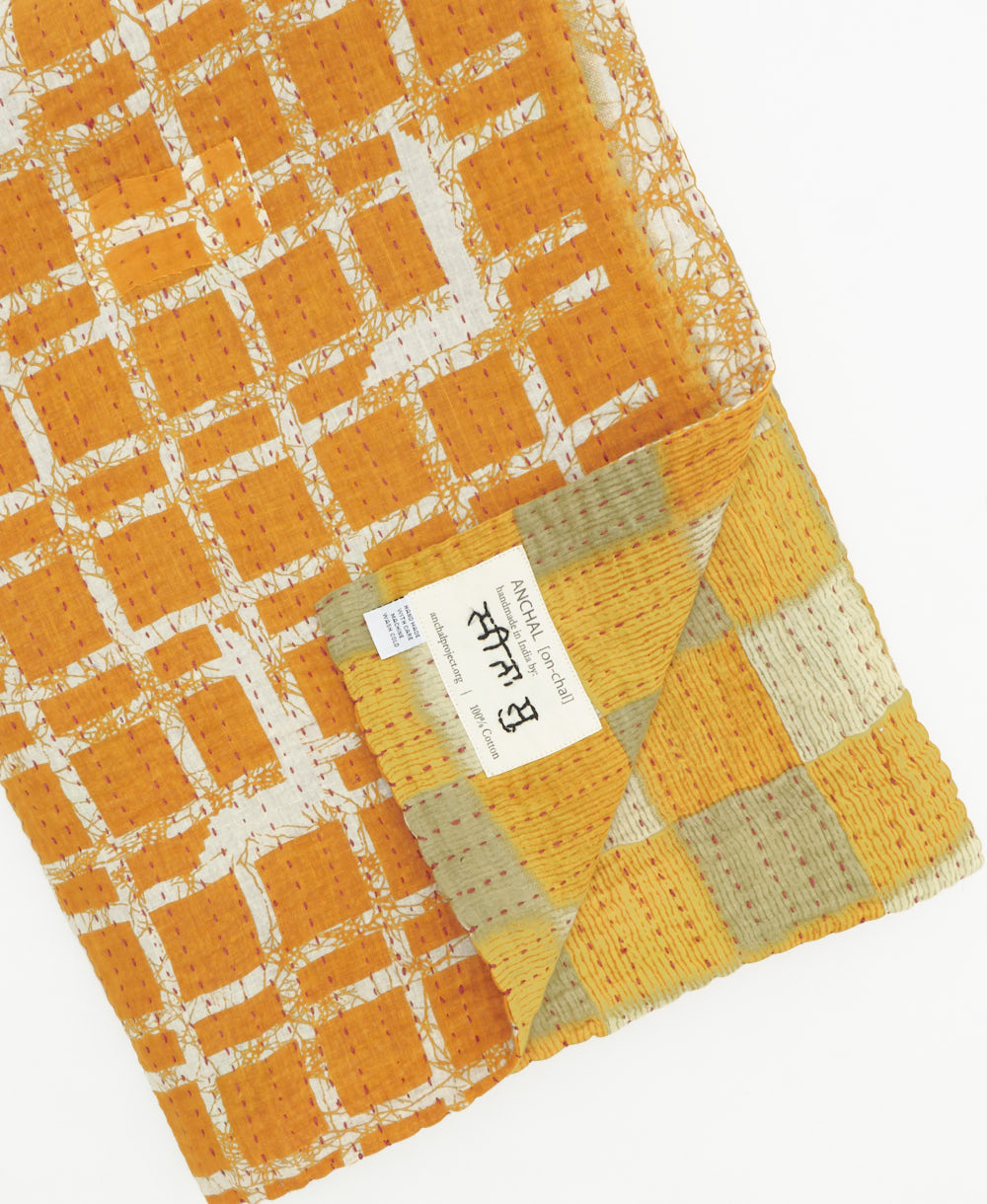 kantha quilt throw with a tag featuring the hand-stitched signature of the maker