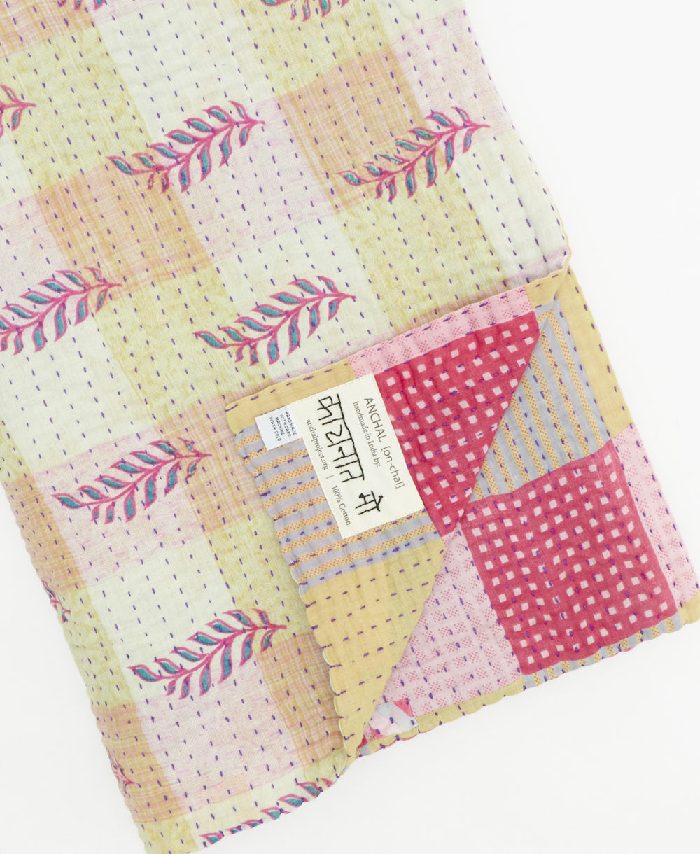 kantha quilt throw with a tag featuring the hand-stitched signature of the maker