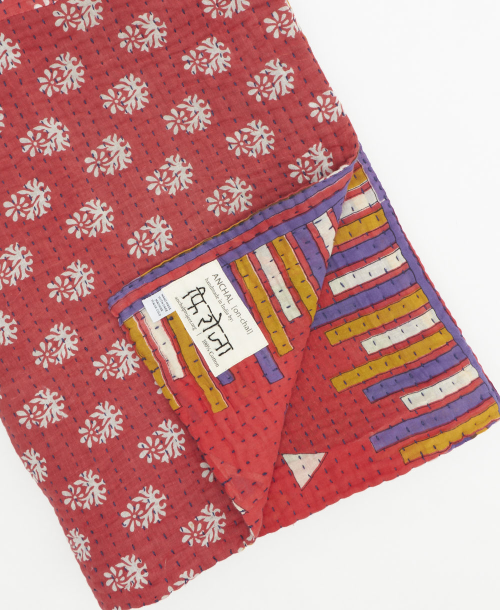 kantha quilt throw with a tag featuring the hand-stitched signature of the maker