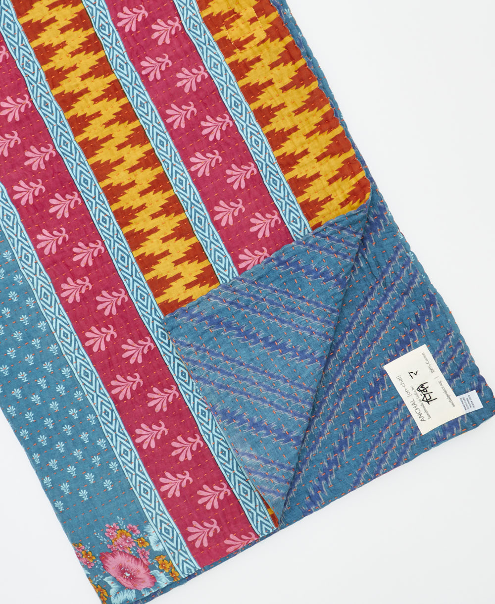 kantha quilt throw with a tag featuring the hand-stitched signature of the maker