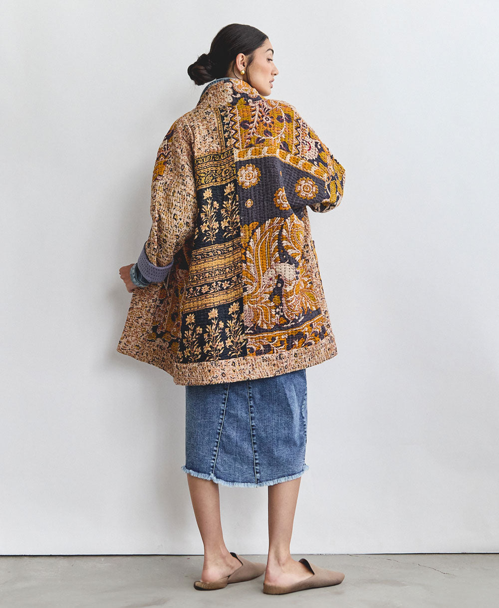 woman wearing a quilted jacket in mustard and navy hues showing off the back of the jacket
