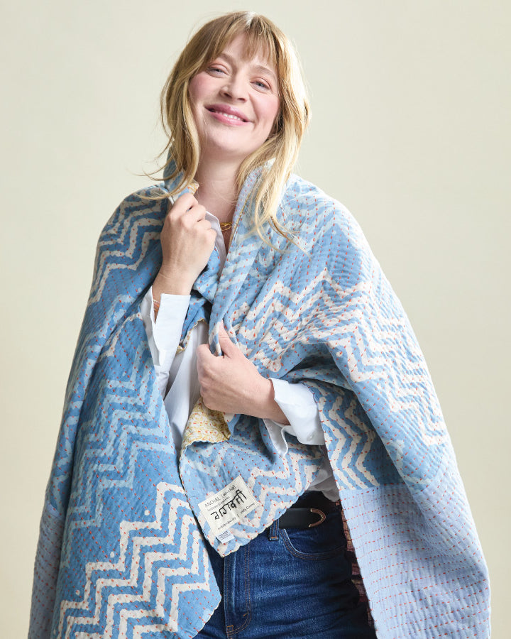 Woman wearing a blue and white patterned kantha quilt over her shoulders against a beige background