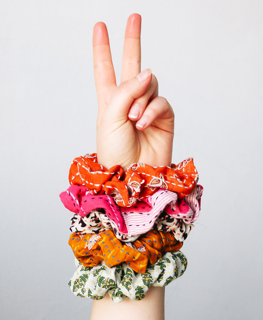 hand holding up a peace sign gesture with unique and colorful cotton scrunchies on the wrist