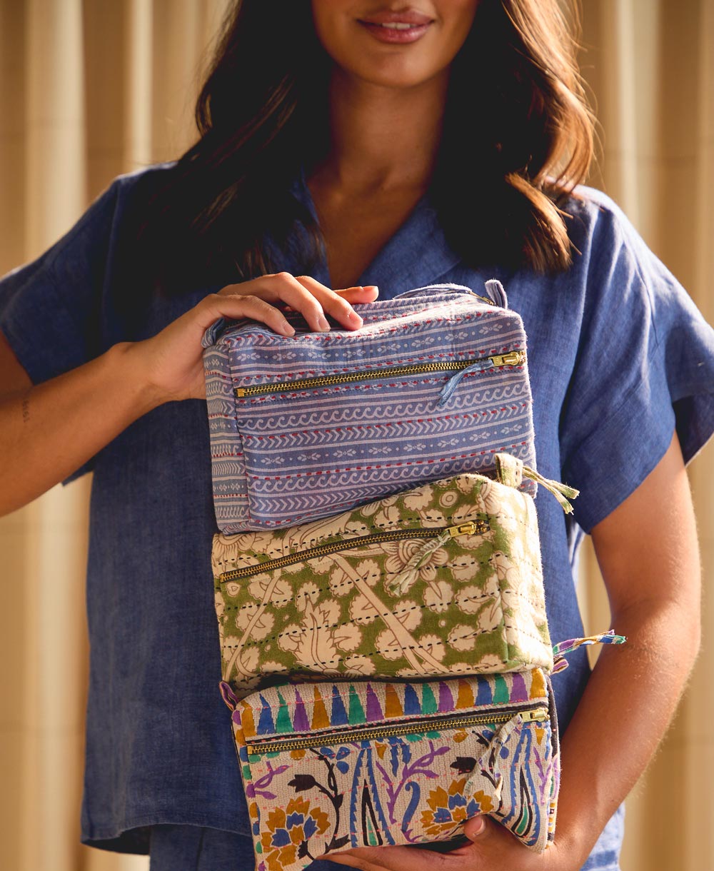 woman holding stack of three patterned toiletry bags