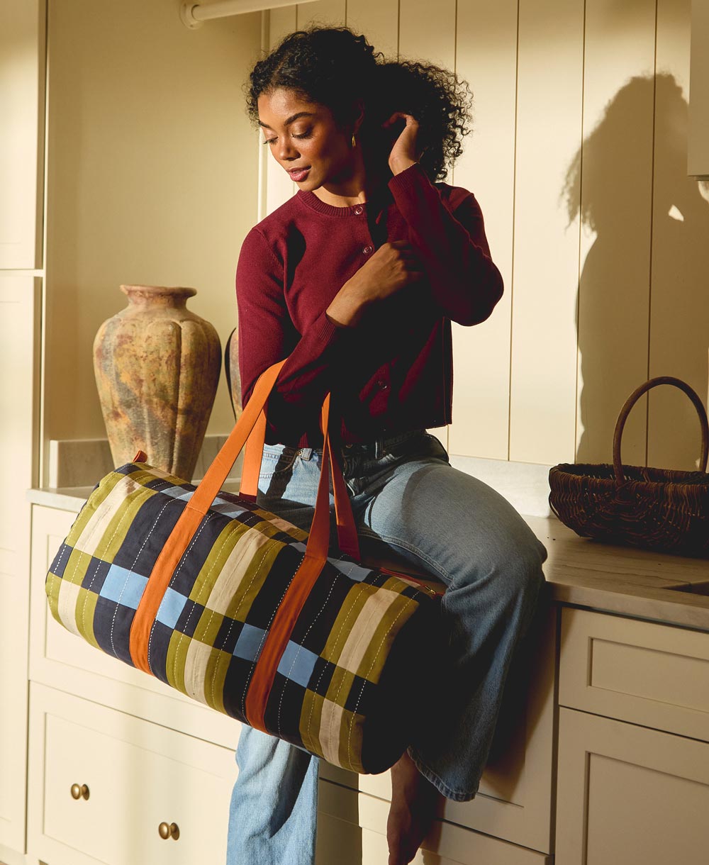 Woman holding a colorful striped weekender duffle bag in a kitchen setting