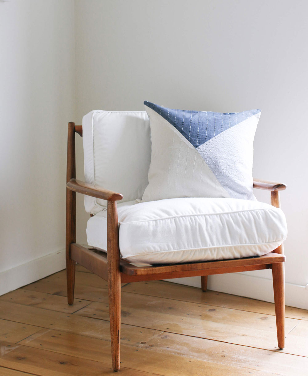 Wooden armchair with white cushion and blue and white patterned pillow against a white wall