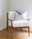 Wooden armchair with white cushion and blue and white patterned pillow against a white wall