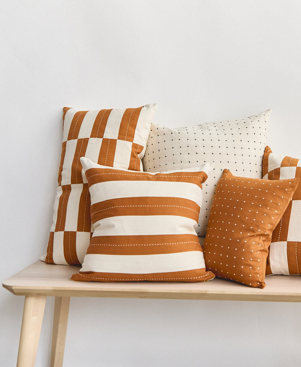 Set of patterned modern throw pillows on a wooden bench against a light gray wall