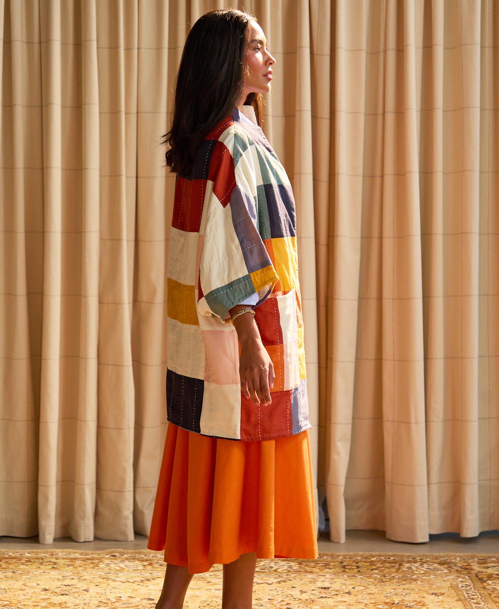 woman standing wearing an orange skirt and quilted colorful cocoon jacket