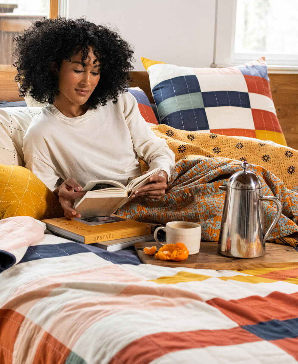Woman reading a book on a cozy bed with a colorful quilt and pillows