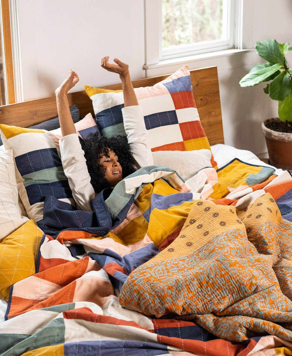 Person lying on a bed with colorful bedding and pillows in a bright room