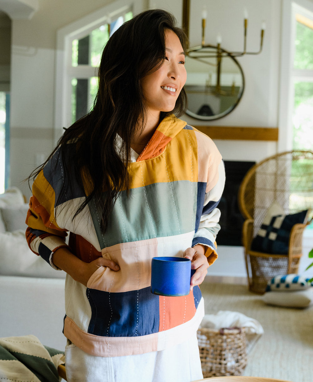 woman wearing colorful checkered quilted hoodie holding cobalt blue ceramic mug