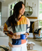woman wearing colorful checkered quilted hoodie holding cobalt blue ceramic mug