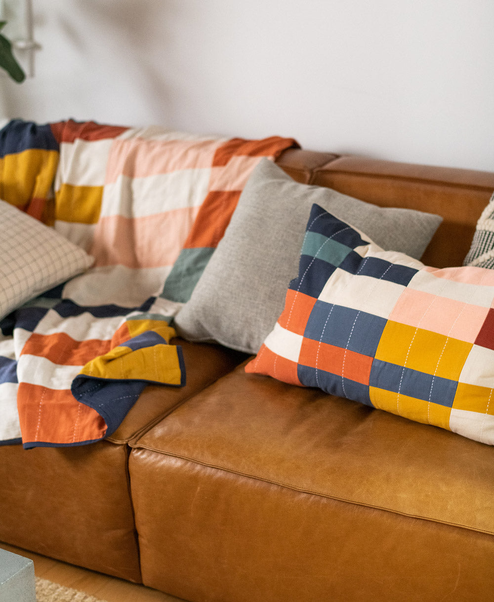 Brown leather sofa with colorful patchwork cushions and blanket