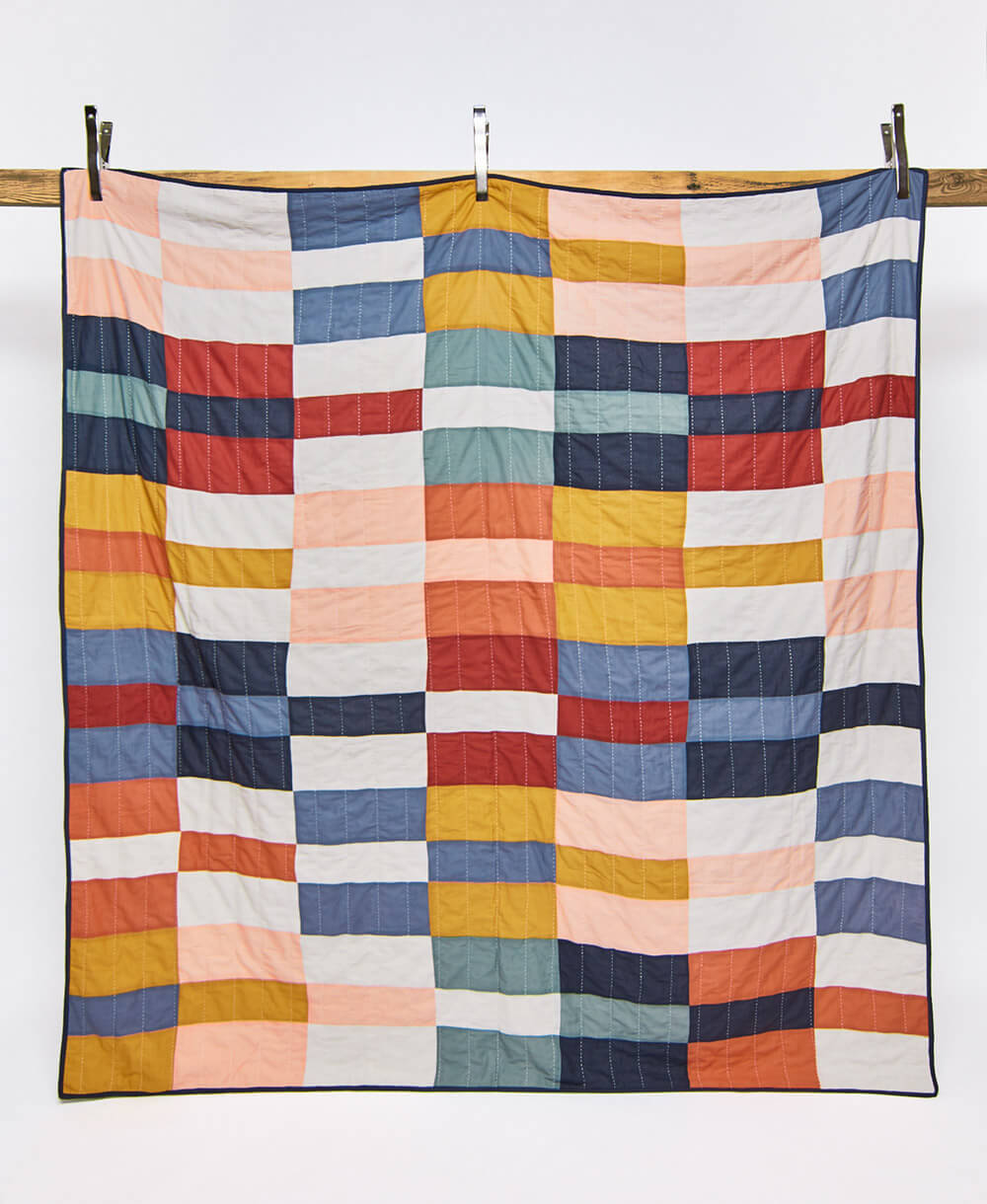 Colorful quilt with a checkered pattern hanging on a wooden rod against a white background