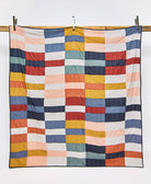 Colorful quilt with a checkered pattern hanging on a wooden rod against a white background