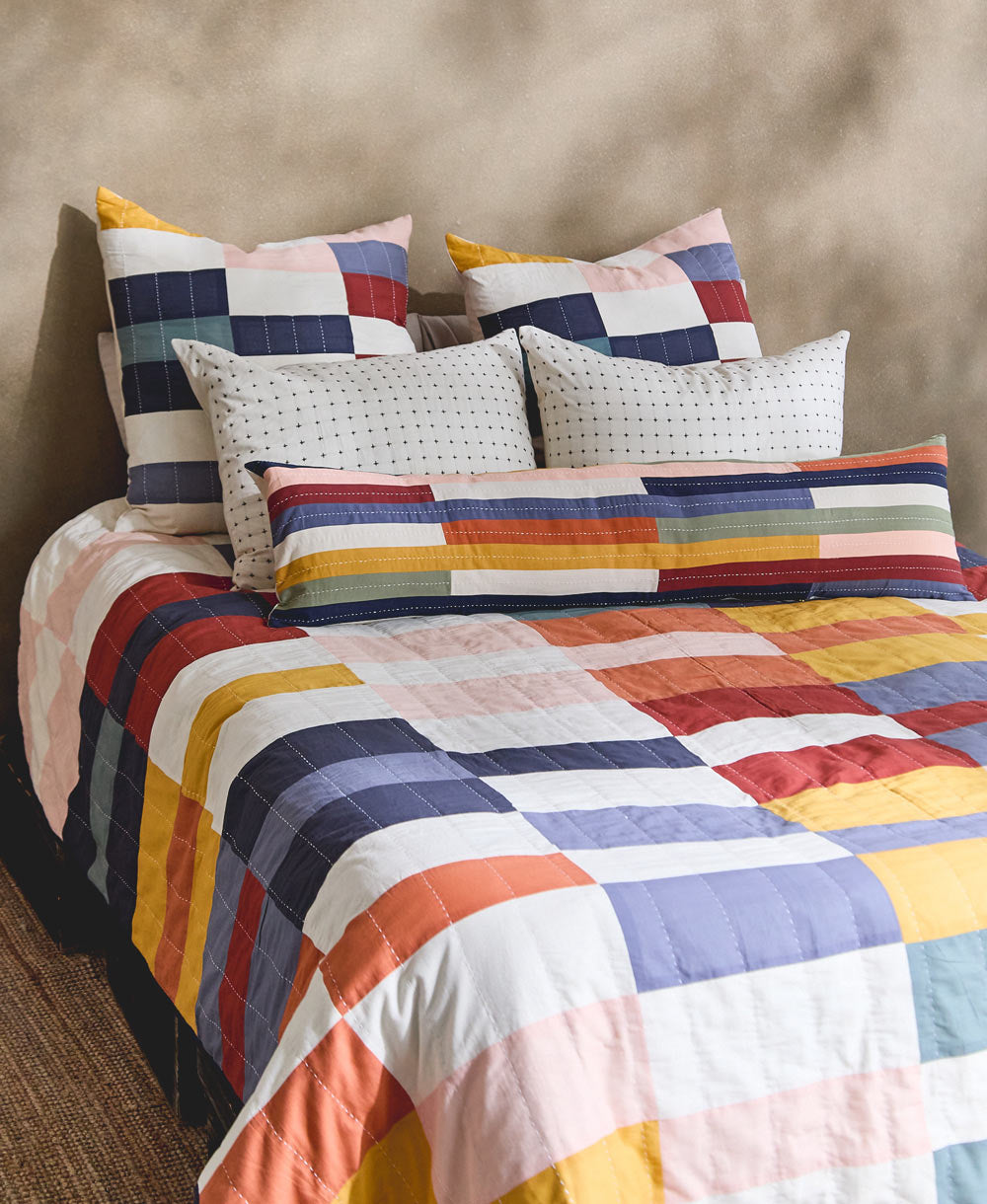 Colorful patchwork quilt with matching pillows on a bed against a beige wall