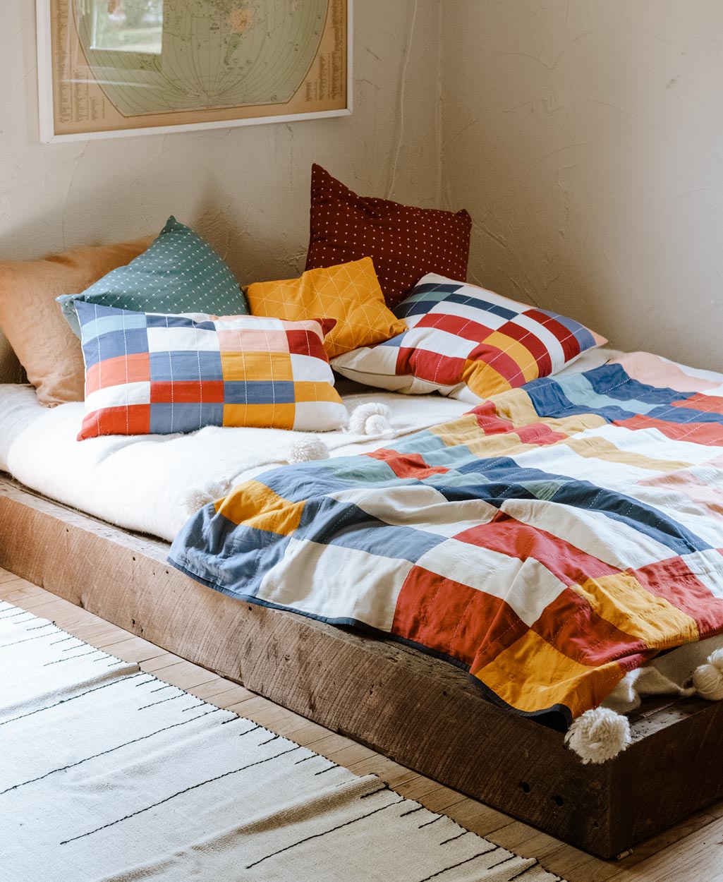 Bed with colorful bedding and pillows in a room with a map on the wall.