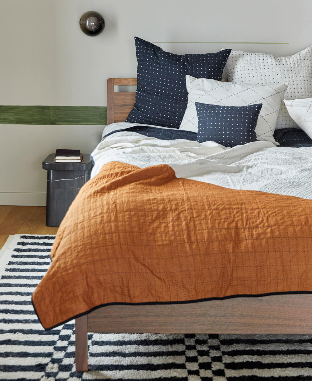 Bed with camel patchwork quilt and patterned pillows in a room with a black and white striped rug