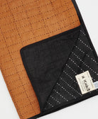 folded naari patchwork quilt with black and camel organic cotton fabrics and tag of artisan signed maker