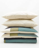 stack of 4 pillows and 1 quilts in tones of green and blue on a white background