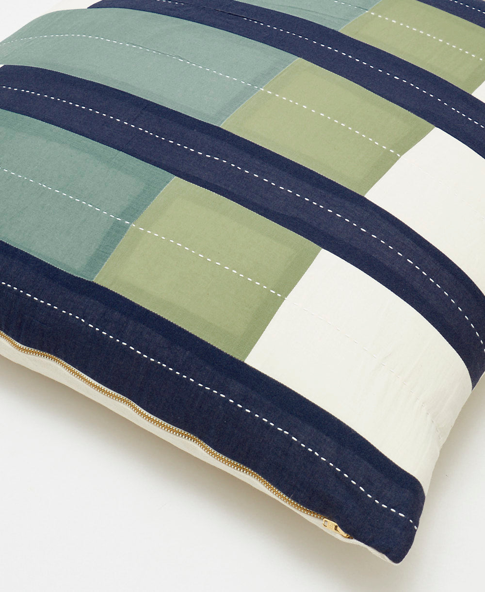 Close-up of a striped pillow with green, blue, and white colors on a light background
